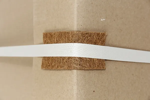 Coir edge protector under a packing strap